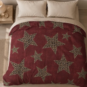 Puede incluir: Una funda nórdica burdeos con un estampado de estrellas con estampado de leopardo. Las estrellas varían en tamaño y están dispersas por la superficie. Se ven dos almohadas de color crema en la parte superior de la cama.