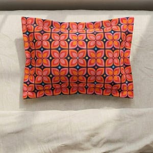 May include: A rectangular pillow with a repeating floral pattern in shades of orange, pink, and blue on a navy blue background. The pillow is centered on a light-colored surface, showcasing its vibrant design.