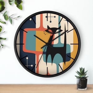 May include: A black-framed wall clock with a retro design. The clock face features a black cat silhouette against a colorful backdrop of orange, blue, and yellow geometric shapes. Black clock hands indicate the time.