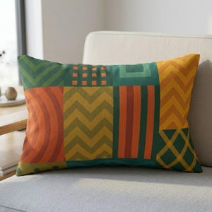 May include: Rectangular decorative pillow with a patchwork design. The pillow features various geometric patterns in shades of green, orange, and yellow. The patterns include stripes, chevrons, and squares. The pillow is placed on a light-colored sofa.