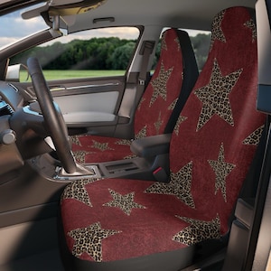 May include: Car seat covers featuring a burgundy backdrop and large leopard print stars. The covers are fitted in a car, with the steering wheel and dashboard visible. The seats have a black backing.