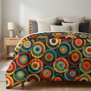 May include: A colorful comforter with a retro design featuring concentric circles in shades of orange, red, teal, and green on a black background. The bedding is placed on a wooden bed frame with several pillows.