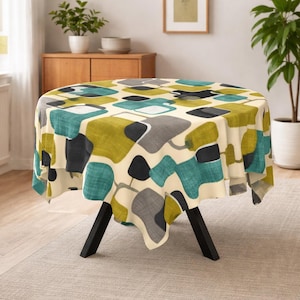 Può includere: Una tovaglia rotonda con un design moderno della metà del secolo. Il tessuto color crema presenta un motivo di forme astratte turchesi, verde oliva, grigie e nere. La tovaglia è drappeggiata su un tavolo con gambe nere.