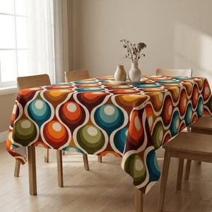 Könnte beinhalten: Ein rechteckiges Tischtuch mit Retro-Design. Das Muster zeigt große, sich überlappende Kreise in Orange-, Braun-, Türkis- und Grüntönen auf cremefarbenem Hintergrund. Das Tischtuch ist über einen Holztisch drapiert.