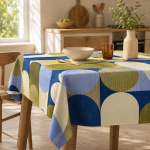 Könnte beinhalten: Eine quadratische Tischdecke mit einem geometrischen Muster aus überlappenden Kreisen in Marineblau, Hellblau, Olivgrün und Creme. Der Stoff hat eine feine vertikale Textur und liegt auf einem Holztisch mit einer hellen Oberfläche.