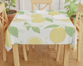 May include: A rectangular tablecloth with a lemon pattern. The design features yellow lemons, green leaves, and white flowers on a light background. The tablecloth is draped over a wooden table with four chairs.