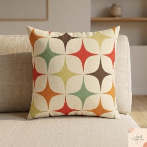 Könnte beinhalten: Ein dekoratives Kissen mit einem Retro-Starburst-Muster in Orange, Rot, Grün, Gelb und Braun auf cremefarbenem Hintergrund. Das Kissen liegt auf einem beigen Sofa und bietet einen Farbtupfer und eine Vintage-Ästhetik.