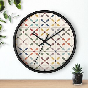 May include: A round wall clock with a black frame. The clock face features a cream-colored background with a repeating floral pattern in various colors, including red, blue, and yellow. Black clock hands indicate the time.