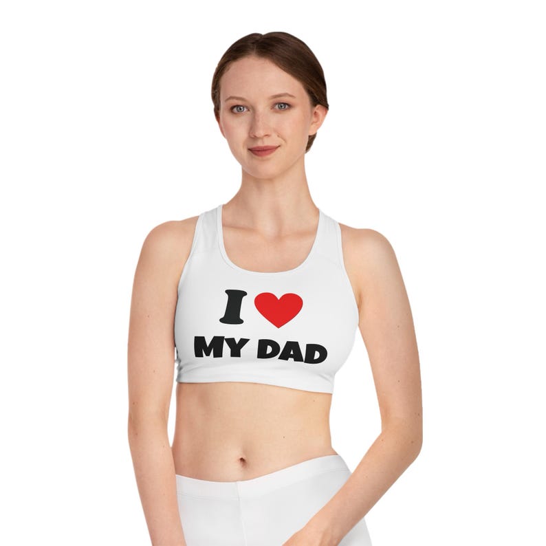 May include: White sports bra with the text "I &hearts; MY DAD" in black and red. The bra has a racerback design and is made of a soft, stretchy material. The bra is designed for low-impact activities.