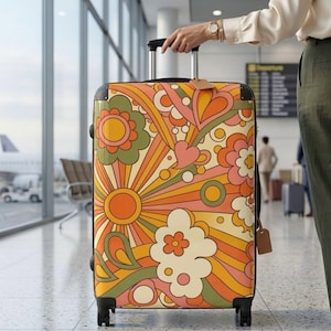 Puede incluir: Una maleta con ruedas con un diseño floral retro en tonos naranja, amarillo, rosa y verde. La maleta se sostiene en un aeropuerto. El diseño incluye flores, corazones y rayos de sol.