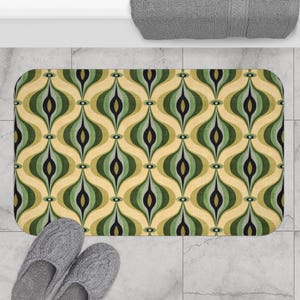 Könnte beinhalten: Eine rechteckige Badematte mit einem Retro-Muster in Grün-, Schwarz- und Beigetönen. Das Design zeigt ein abstraktes, sich wiederholendes Motiv aus länglichen Ovalen. Graue Hausschuhe sind unten links zu sehen.
