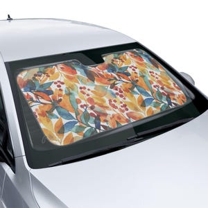 May include: A car windshield sunshade featuring a colorful watercolor pattern of leaves and berries in shades of orange, yellow, blue, and red. The sunshade is designed to fit the windshield of a car.