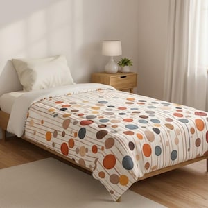 Könnte beinhalten: Ein Einzelbett mit einer cremefarbenen Bettdecke mit einem Muster aus bunten Kreisen und vertikalen Linien. Die Kreise sind in Orange-, Braun-, Blau- und Gelbtönen gehalten. Ein weißes Kissen und ein cremefarbener Teppich sind ebenfalls zu sehen.