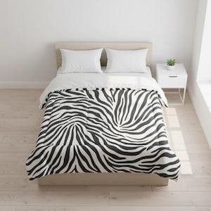 Pode incluir: Uma cama com um edredom com estampa de zebra. O edredom apresenta um padrão em preto e branco, com duas almofadas brancas e um lençol branco. Uma pequena mesa de cabeceira branca com uma planta fica ao lado da cama.