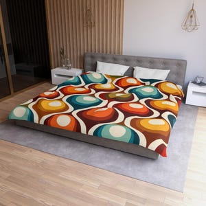May include: A duvet cover featuring a repeating pattern of rounded, organic shapes in shades of orange, yellow, teal, and brown, separated by white outlines. The bedding is draped over a bed with a gray upholstered headboard and two white pillows.