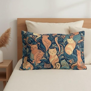 Puede incluir: Un cojín rectangular con un diseño de gatos. El cojín presenta gatos estilizados en tonos naranja, amarillo y azul sobre un fondo azul oscuro. Los gatos están rodeados de formas orgánicas onduladas.