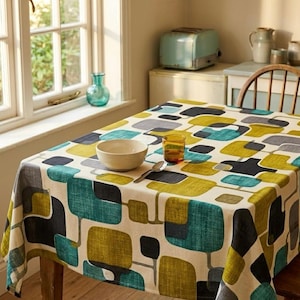 May include: A rectangular tablecloth with a retro geometric pattern in teal, yellow, grey, and black. The tablecloth is on a wooden table, with a bowl, glass, and spoon on top. A window and a vintage toaster are in the background.
