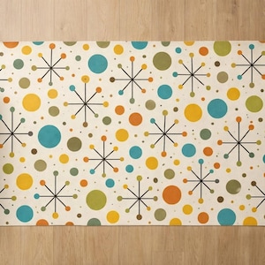 Puede incluir: Una alfombra rectangular con un diseño moderno de mediados de siglo. La alfombra presenta un fondo crema con un patrón de círculos coloridos y formas de estrellas en tonos de amarillo, naranja, azul y verde. La alfombra está colocada sobre un suelo de madera.