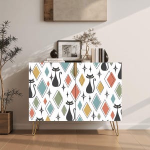 May include: A white cabinet with a mid-century modern design. The cabinet features a repeating pattern of black cat silhouettes, diamonds in various colors, and starbursts. It has gold hairpin legs and a gold handle.