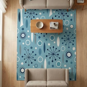Op de afbeelding: Lichtblauw vloerkleed met een mid-century modern design met witte, marineblauwe en grijze geometrische vormen. Het kleed ligt onder een houten salontafel en twee beige banken, waardoor een woonkamer ontstaat.