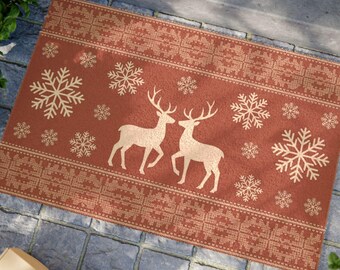 May include: A rectangular doormat with a festive design. The mat features a red background with cream-coloured snowflakes and two deer facing each other. The border has a patterned design. A seasonal home decor item.