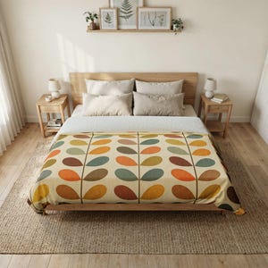 May include: A bed featuring a cream-colored blanket with a repeating pattern of stylized leaves in shades of orange, yellow, brown, and teal. The bed is dressed with four light gray pillows and sits on a wooden frame in a bedroom setting.