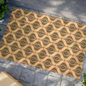 Könnte beinhalten: Eine rechteckige Fußmatte mit einem sich wiederholenden Muster aus stilisierten Tropfenformen in Beige-, Braun- und Olivgrüntönen. Die Matte liegt auf einer grauen Steinoberfläche, was auf eine Umgebung im Freien hindeutet.