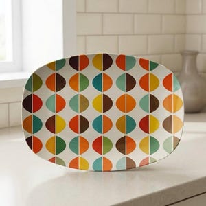 Può includere: Un vassoio rettangolare da portata con un design retrò. Il vassoio presenta un motivo di forme a semicerchio colorate in tonalità di arancione, giallo, marrone, verde acqua e rosso su sfondo bianco. Il vassoio è in ceramica ed è adatto per servire cibo.