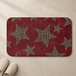 May include: A burgundy bath mat with a repeating pattern of leopard print stars. The stars are of varying sizes and are spread across the mat. The mat has rounded corners and a textured finish, adding a touch of rustic charm to any bathroom, measuring approximately 90cm x 60cm.