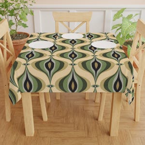 May include: A rectangular tablecloth with a retro, geometric pattern in shades of green, black, and beige. The design features an abstract, teardrop-like motif. Three white plates sit on the table, which is surrounded by wooden chairs.