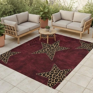 May include: A burgundy outdoor rug featuring large star patterns with a leopard print design. The rug is placed on a tiled patio, with two beige sofas and a small wooden table in the background.