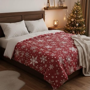 Pode incluir: Uma cama com travesseiros brancos e um edredom vermelho com um padrão de flocos de neve brancos. A cama é feita com um lençol branco e um edredom vermelho com um desenho de floco de neve. Uma árvore de Natal está ao fundo.