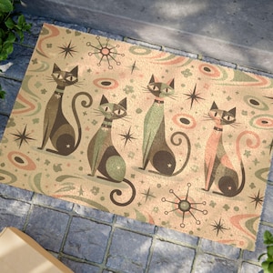 Könnte beinhalten: Rechteckige Fußmatte mit vier stilisierten Katzen in Braun-, Grün- und Rosatönen, jeweils mit Halsband. Der beige Hintergrund ist mit Sternen, Kreisen und floralen Elementen verziert. Für den Eingangsbereich.