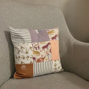 May include: A patchwork cushion with diverse fabric patterns and animal illustrations. The cushion features stripes, bunnies, giraffes, zebras, and an elephant. The colour palette includes white, brown, lavender, and peach. The word "lovely" is printed on the cushion.