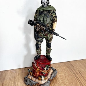 May include: A detailed figurine of a soldier in camouflage attire, holding a rifle. The figure has a skull mask and stands atop a red barrel with the word "FUEL" visible. The base includes a timer and other military-themed details.