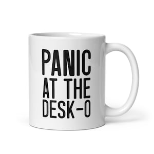 May include: White ceramic mug with the text "PANIC AT THE DESK-0" in bold black letters. The mug has a curved handle and a glossy finish. A humorous office-themed item.