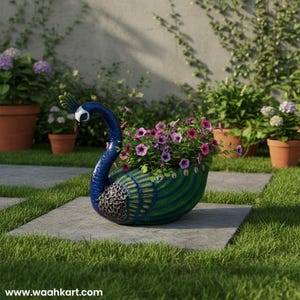 Puede incluir: Una maceta con forma de pavo real, pintada en tonos azules y verdes, que contiene vibrantes flores rosas. La maceta está colocada sobre un camino de piedra en un jardín, con otras plantas en macetas visibles en el fondo. La dirección del sitio web "www.waahkart.com" es visible en la parte inferior.