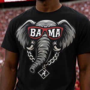 Könnte beinhalten: Schwarzes T-Shirt mit einem grauen Elefantenkopf, der eine rote Sonnenbrille mit der Aufschrift "BA MA" trägt. Der Elefant hat eine silberne Halskette mit einem rautenförmigen Anhänger mit dem Buchstaben "A".