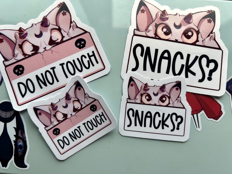 Puede incluir: Un conjunto de pegatinas con una criatura de dibujos animados con cuernos y una luna creciente. Las pegatinas muestran las frases "DO NOT TOUCH" y "SNACKS?" en texto negro sobre un fondo blanco.