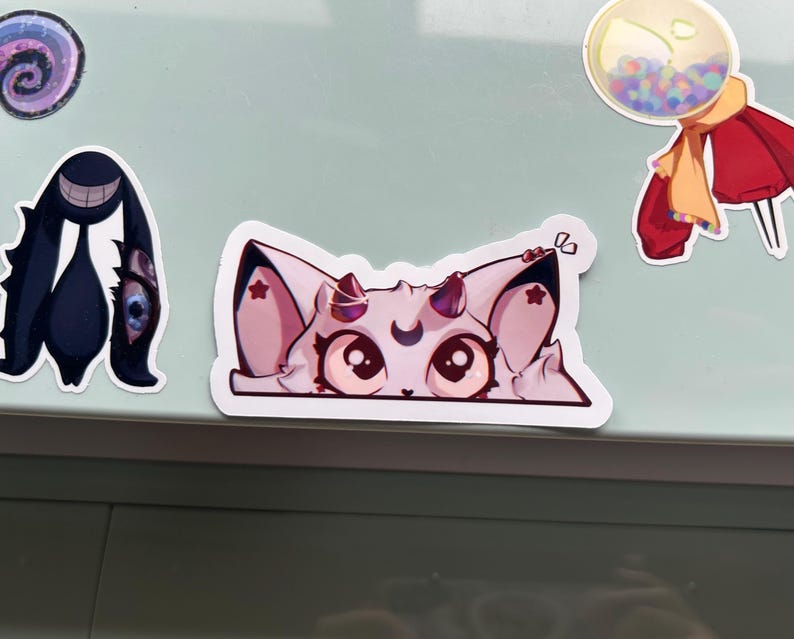Puede incluir: Una colecci&oacute;n de pegatinas coloridas sobre una superficie verde claro. Las pegatinas incluyen un gato de dibujos animados con pelaje rosa y blanco, una criatura negra con una cara sonriente, un dise&ntilde;o en espiral y una m&aacute;quina de chicles.
