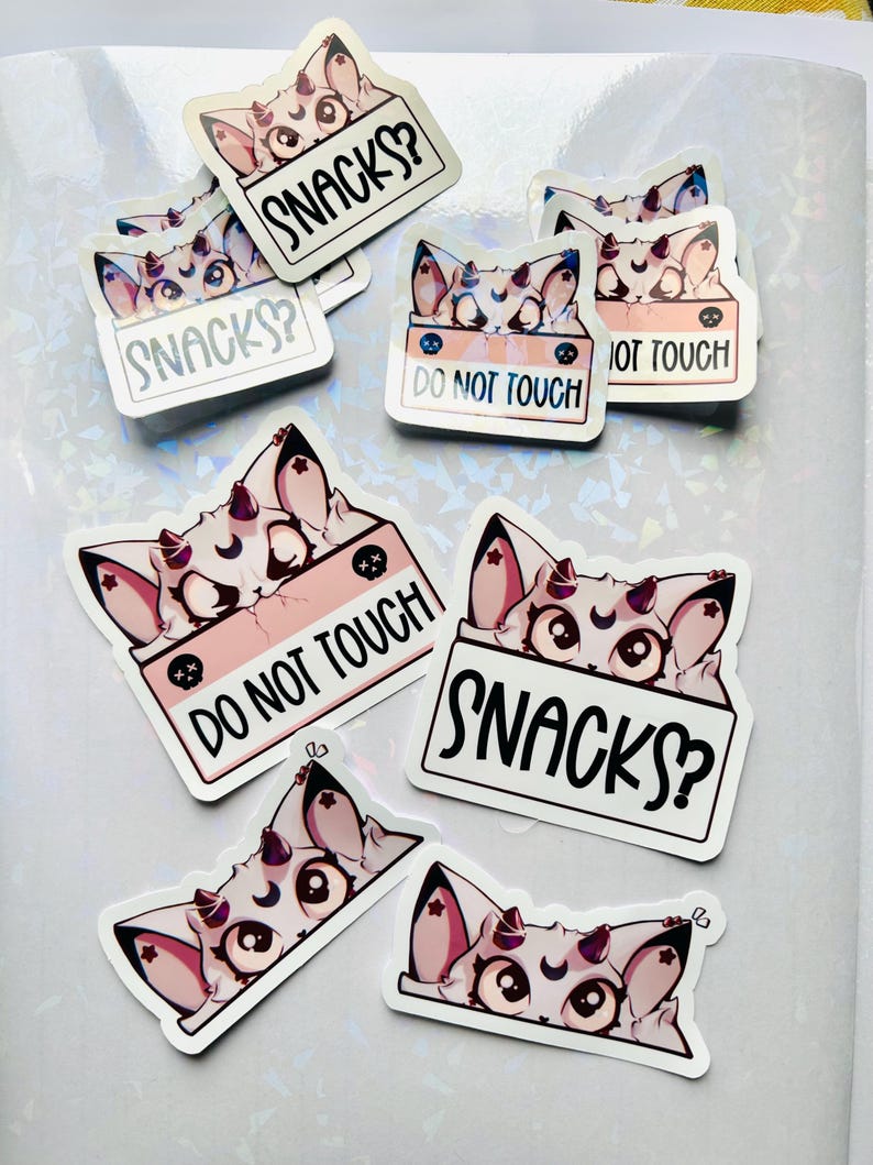 Puede incluir: Un conjunto de pegatinas con un gato de dibujos animados con cuernos y una luna creciente en la frente. Algunas pegatinas tienen el texto "SNACKS?" y otras "DO NOT TOUCH". Las pegatinas son blancas con detalles en rosa y negro.