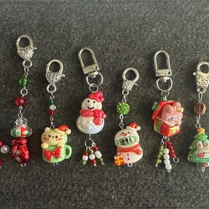 May include: A selection of festive keyrings with Christmas-themed charms. The keyrings showcase various designs, such as a Christmas tree, snowman, and a cat in a mug. They are decorated with red, green, and white beads, and silver-tone clasps.