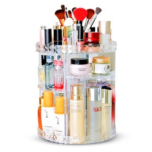 May include: A clear, rotating makeup organiser filled with various cosmetics and brushes. The organiser has multiple tiers and compartments, showcasing lipsticks, skincare products, and makeup tools. The clear design allows for easy visibility of the contents.
