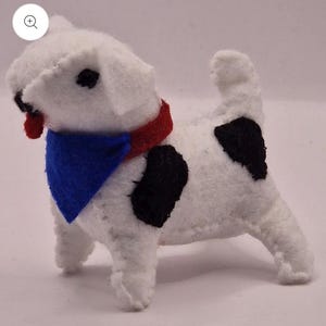 May include: A handmade white felt dog with black spots, a red collar, and a blue bandana. The dog has black eyes and a red tongue. This plush toy is a charming decorative item.
