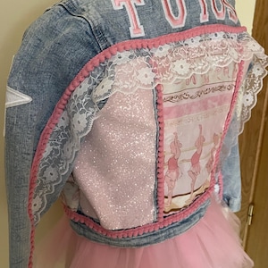 May include: A light blue denim jacket with the word "TUTUS" in pink lettering on the back. The jacket features pink lace and pom-pom trim, a pink glitter panel, and a pink tutu skirt.