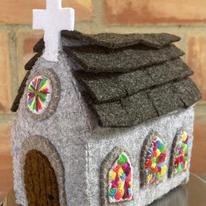 以下が含まれることがあります： 白い十字架が付いた、手作りの灰色のフェルト教会。茶色の木のドア、灰色の屋根瓦、カラフルな刺繍のステンドグラスの窓が特徴です。装飾品です。