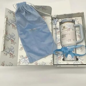Puede incluir: Un juego de regalo con un vaso blanco y dorado con asa, una pajita azul y una cinta azul. El vaso est&aacute; decorado con motivos florales y las palabras "ENCHER TUMBLER". El juego incluye una bolsa con cord&oacute;n azul y est&aacute; empaquetado en una caja con estampado floral.