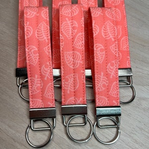 May include: Five pink keychains with silver key rings. Each keychain has a white leaf pattern.