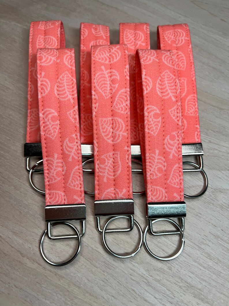 May include: Five pink keychains with silver key rings. Each keychain has a white leaf pattern.