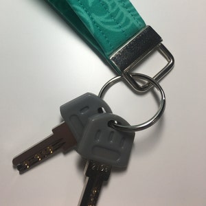 May include: A teal fabric keychain with a silver ring and two gray keys. One key has the number 2106 printed on it.